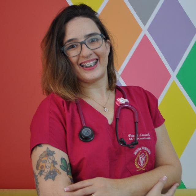 Foto de perfil da Médica Veterinária Paula Lucas, ela está sorrindo e usando um pijama cirurgico com o estetoscópio no pescoço